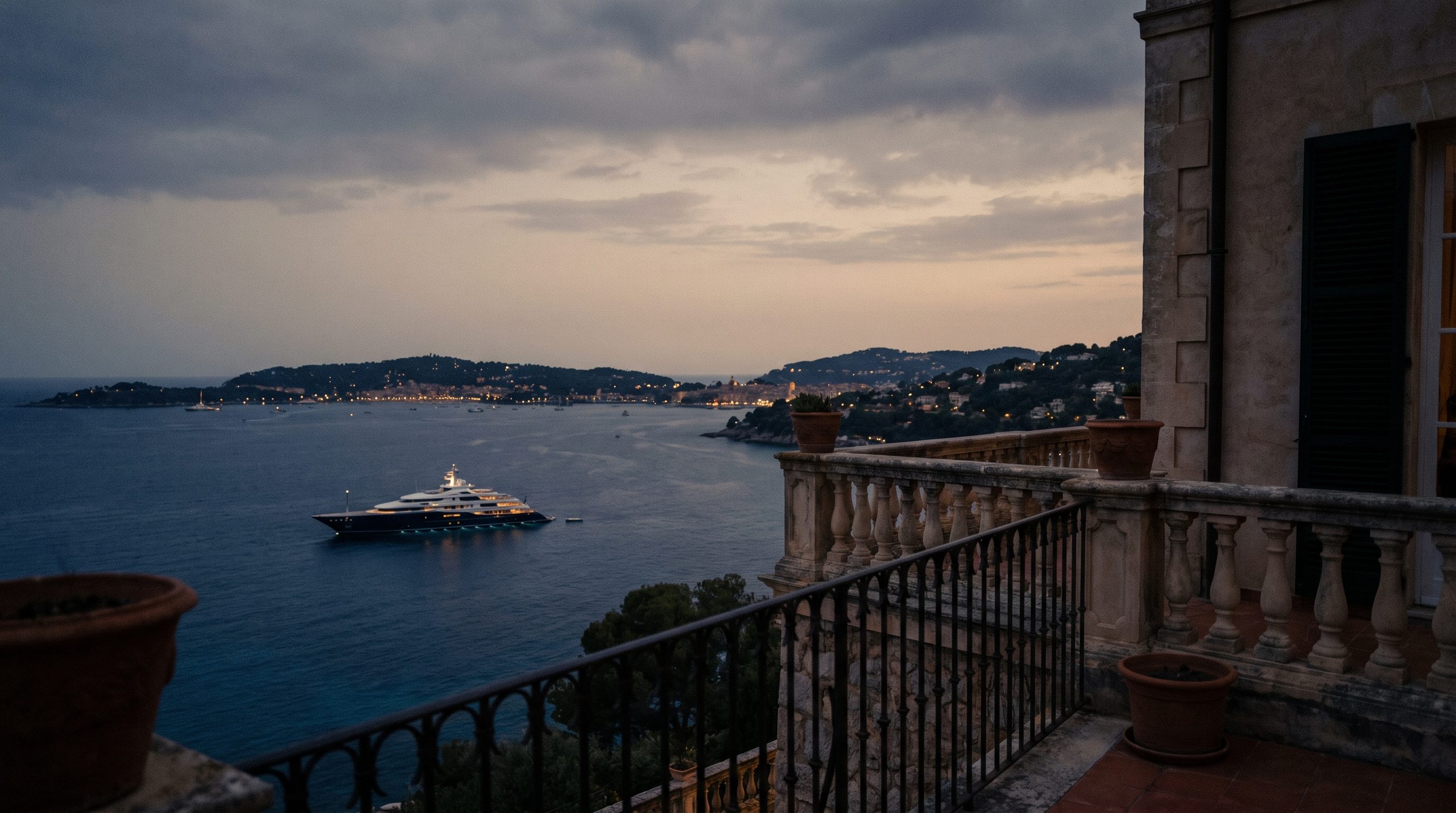 A superyacht at anchor in a Mediterranean bay, seen from a villa terrace at dusk